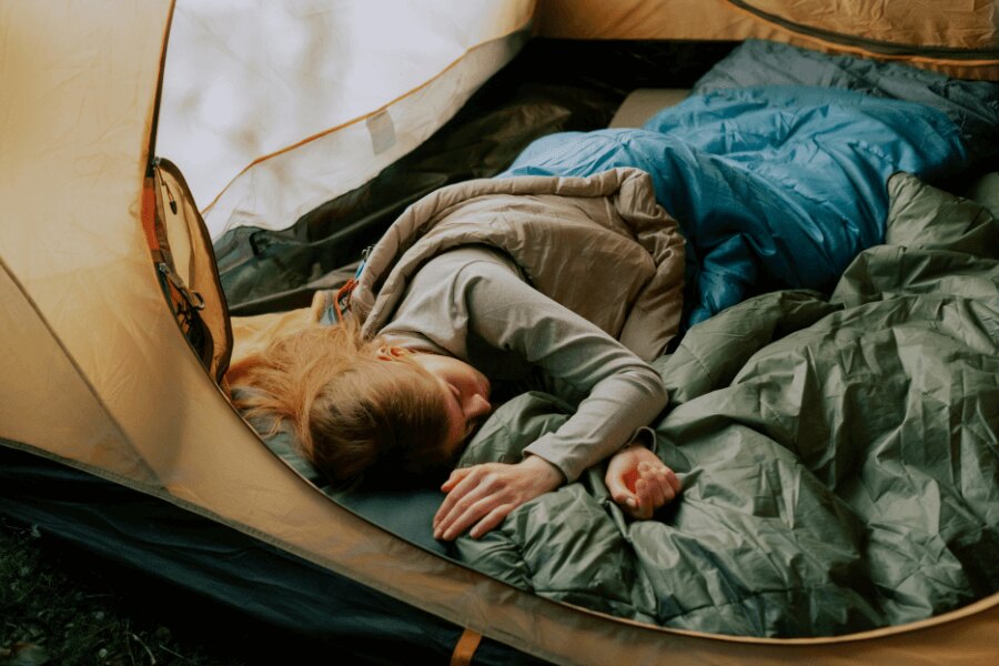 Femeia doarme într-un sac de dormit într-un cort deschis. Sursa: https://www.pexels.com/cs-cz/foto/osoba-zena-kempovani-spani-5994748/