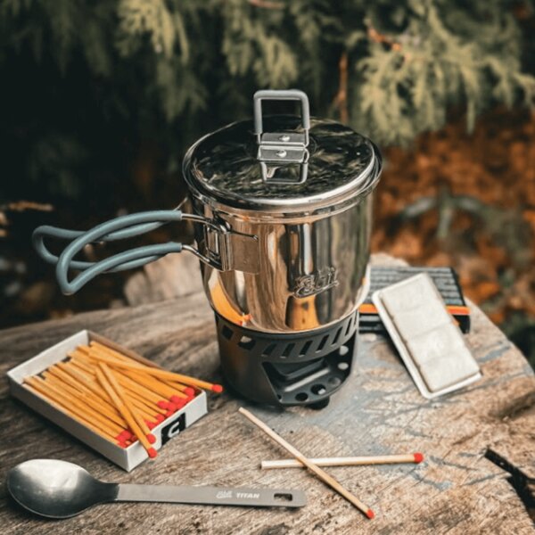 Arzător de titan Esbit cu vas și chibrituri pe o bază de lemn în pădure. Foto: Rigad