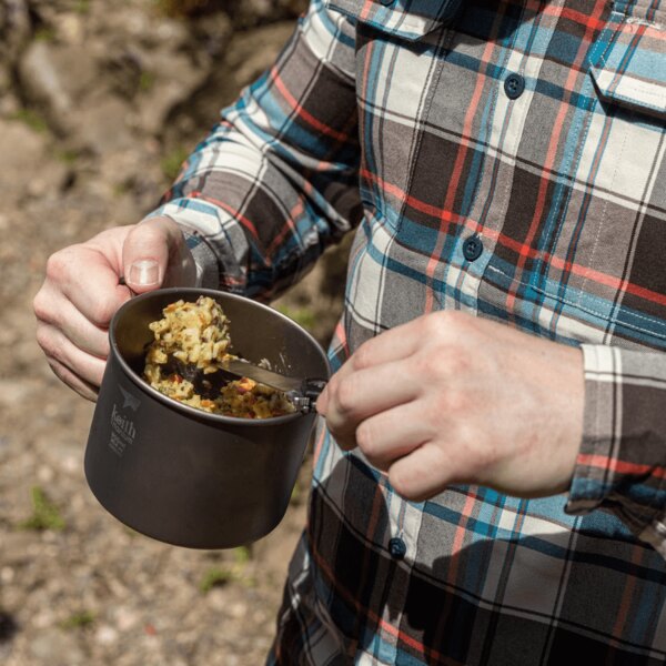 Cană de titan Keith cu mâncare în mână în timpul unei activități în aer liber. Foto: Rigad