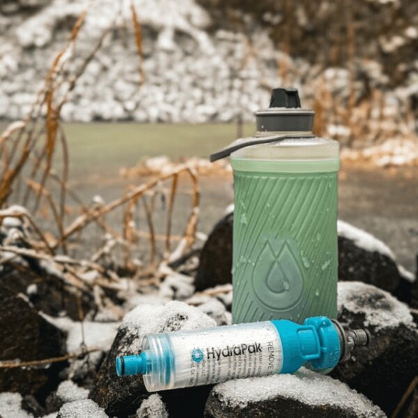Hydrapak sticlă și filtru de apă așezate pe zăpadă. Sistem de hidratare outdoor în mediu de iarnă. Foto: Rigad