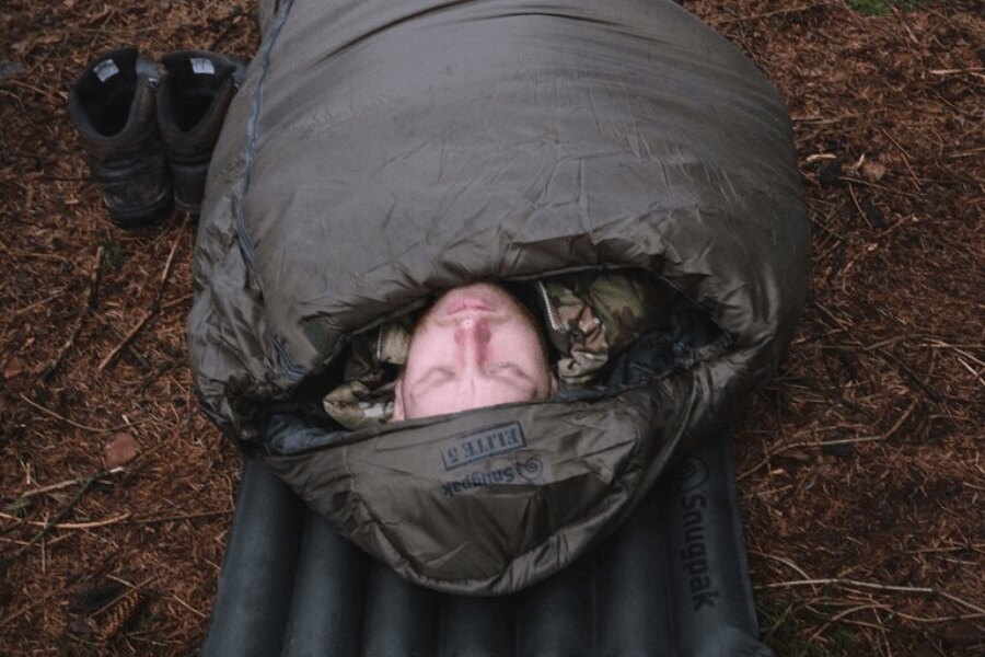 Bărbatul în ținută de camuflaj stă întins pe o saltea gonflabilă în sacul de dormit Softie® Elite 5 Snugpak®. Sursa: Rigad, Snugpak