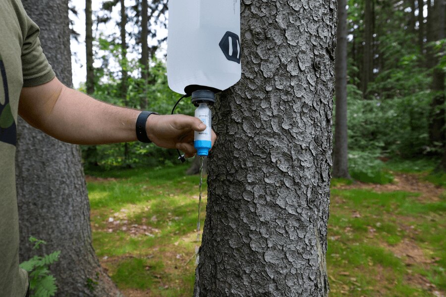 Un filtru de apă gravitațional suspendat de un copac în timpul filtrării apei în natură. Foto: Rigad