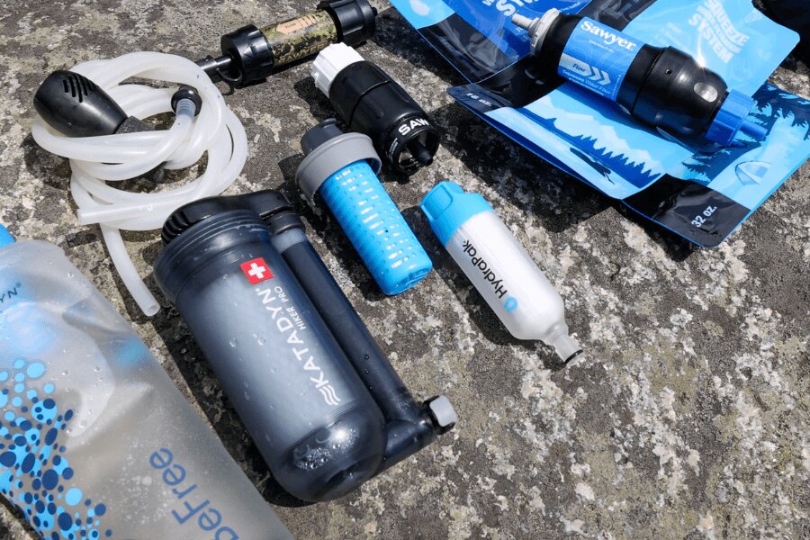 Un set de filtre de apă portabile Sawyer, HydraPak și Katadyn pe un suport de piatră. Foto: Rigad