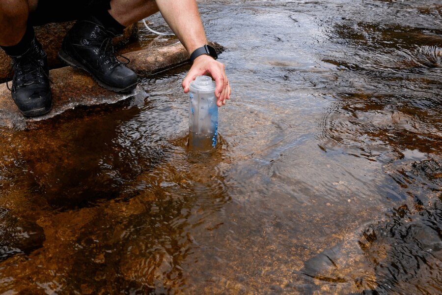 Persoana colectează apă din pârâu într-o sticlă moale cu filtru squeeze în timpul unei expediții în aer liber. Foto: Rigad