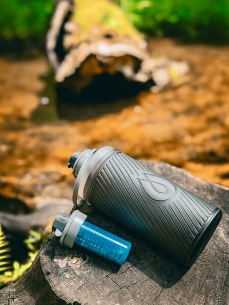 Sticlă Flux HydraPak cu filtru Cap plasată pe un ciot în natură, ideală pentru călătorii și activități outdoor. Foto: Rigad