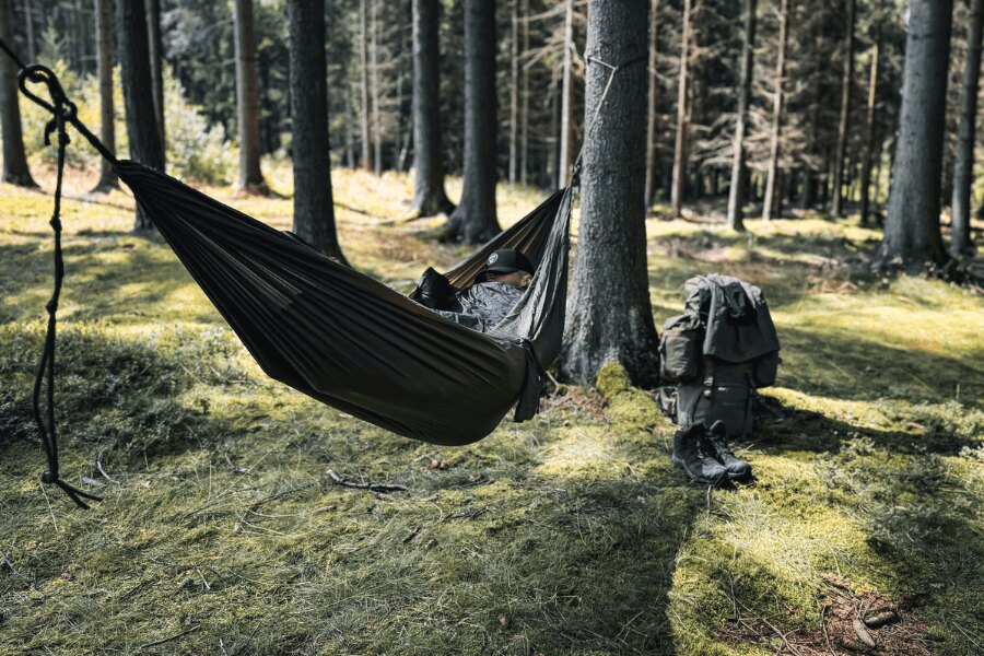 Un hamac folosit ca sistem de dormit în pădure, echipament outdoor și un rucsac pregătit lângă hamac. Foto: Rigad
