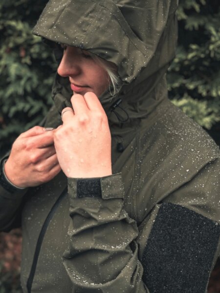 O femeie într-o jachetă impermeabilă Helikon-Tex Squall cu picături de apă pe glugă și mâneci.
