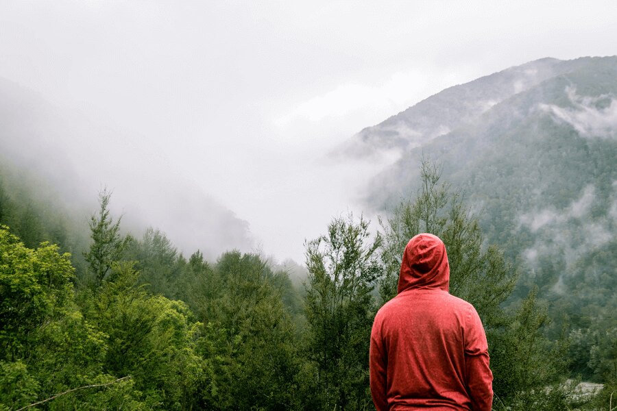 bărbat într-un hanorac roșu stă pe munte în ploaie. Sursa: https://www.pexels.com/cs-cz/foto/395242/