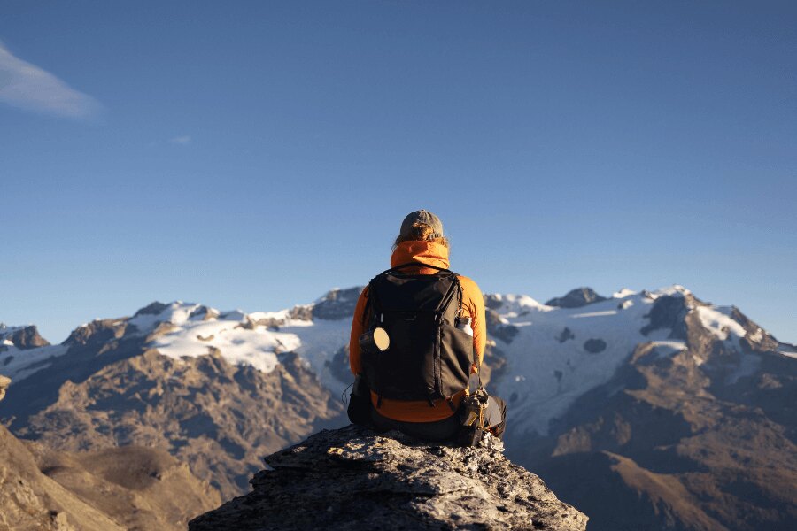 Un bărbat într-o geacă galbenă cu un rucsac stă pe munți. Sursă: https://www.pexels.com/cs-cz/foto/ryma-studeny-ledovec-snih-20220328/