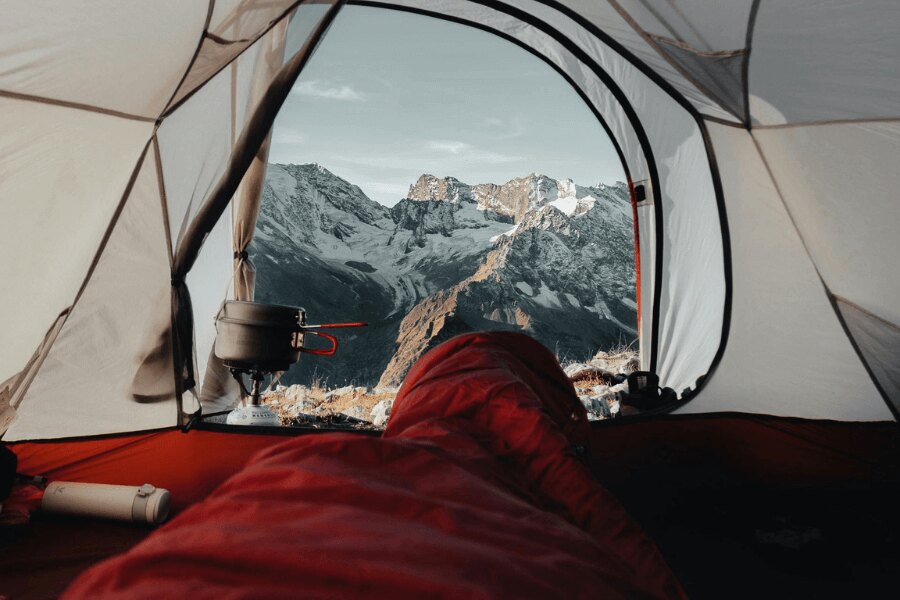Priveliștea dintr-un sac de dormit roșu spre munții înzăpeziți. Sursa: https://www.pexels.com/cs-cz/foto/krajina-hory-cestovani-dobrodruzstvi-9166687/