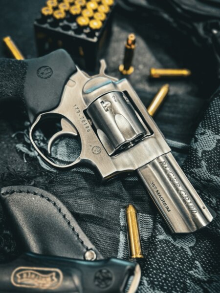 Revolver Ruger GP100 de calibru .357 Magnum așezat lângă gloanțe și toc de tragere.