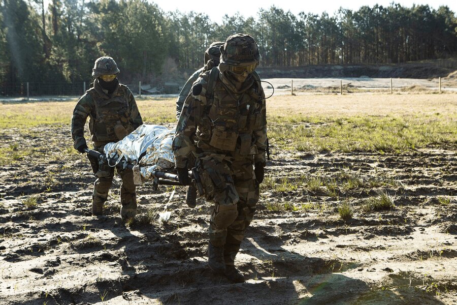Soldații poartă un rănit pe o targă acoperit cu o folie izotermică. Sursa: https://upload.wikimedia.org/wikipedia/commons/4/48/Dutch_Troop_Attack_160322-M-BZ307-198.jpg