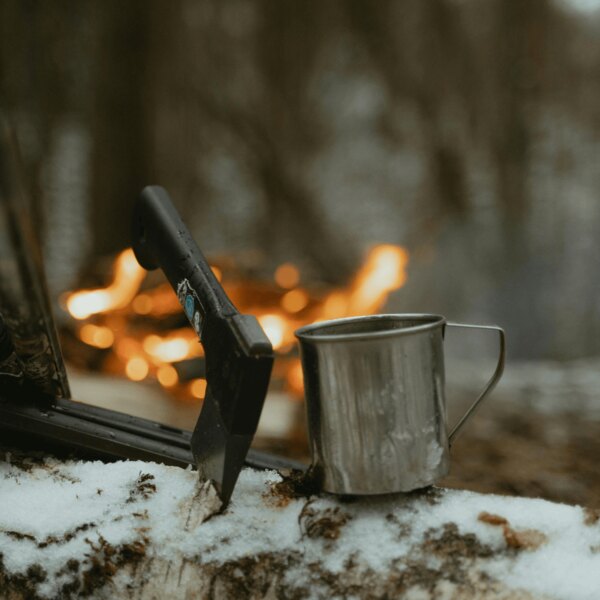 Topor pentru bushcraft și cană de tablă în pădure lângă foc. Sursă: https://www.pexels.com/cs-cz/foto/ryma-studeny-snih-priroda-6204650/