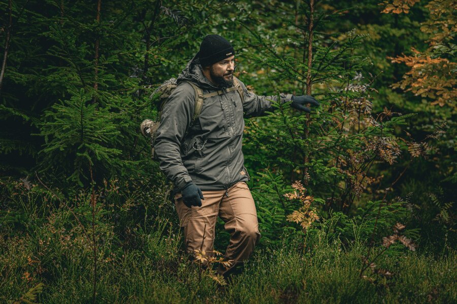 Bărbat în pădurea de toamnă într-o jachetă de iarnă gri Yukon cu izolație Climashield™ Apex® de la Helikon-Tex®, purtând o căciulă și mănuși, cu un rucsac; un exemplu de stratificare corectă și un strat exterior de protecție împotriva umezelii și vântului. Foto: Rigad