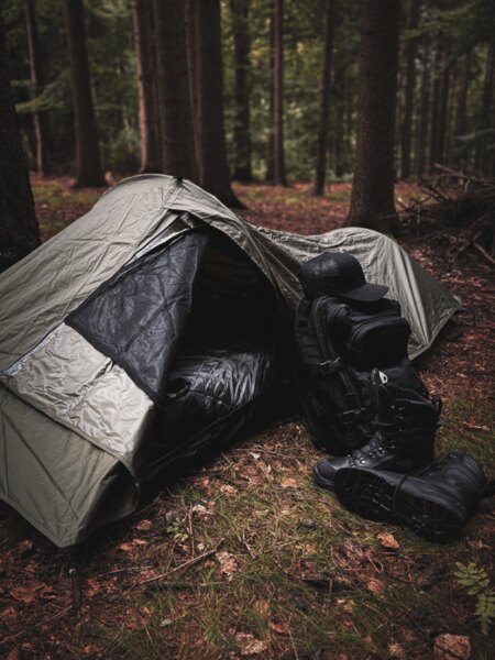 Sac de bivouac Snugpak cu sacul de dormit desfăcut, lângă el rucsacul și bocancii de iarnă, pregătite pentru un adăpost de urgență în natură. Foto: Rigad