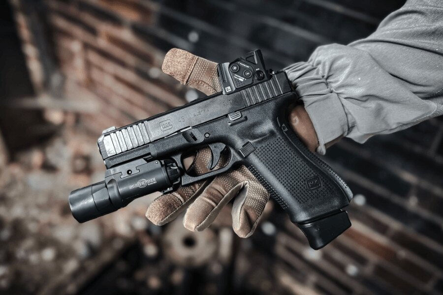 Pistolă Glock 45 cu colimator Aimpoint COA și lanternă pentru armă în mâna trăgătorului. Foto: Rigad