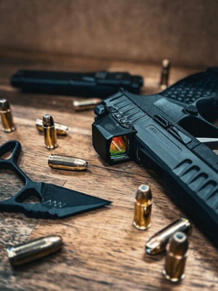 Pistol SIG Sauer cu colimator pe închizător, așezat pe o masă de lemn între gloanțe de 9 mm. Foto: Rigad