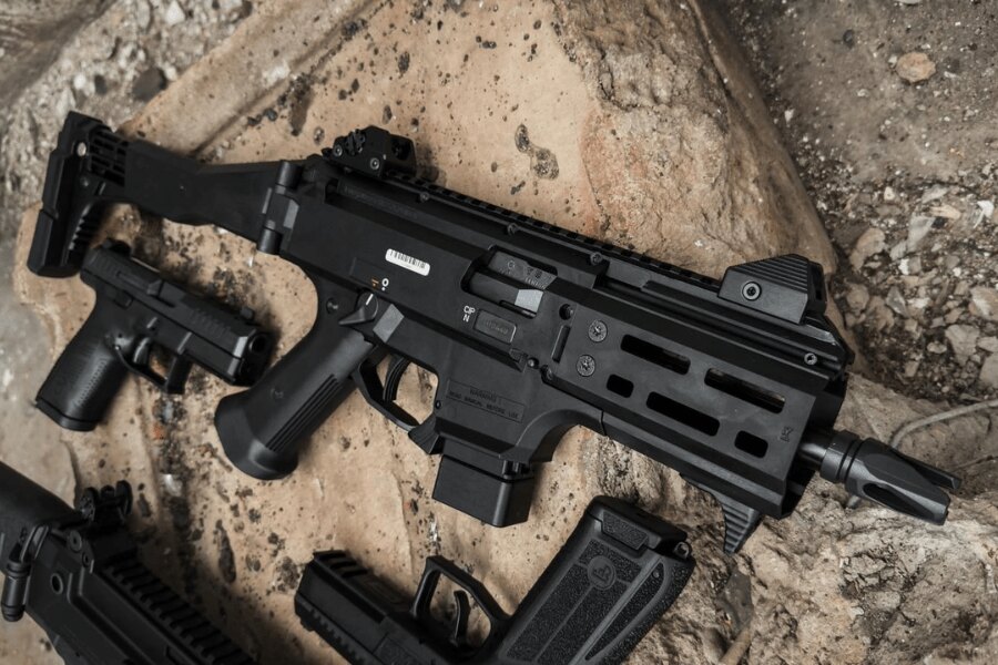 Moderna mitralieră CZ Scorpion EVO 3 cu colimator și pat telescopic așezată pe pământ lângă pistoale și încărcătoare. Foto: Rigad