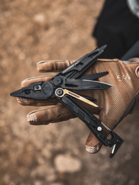 Multitool Leatherman MUT desfăcut în palmă într-o mănușă tactică.