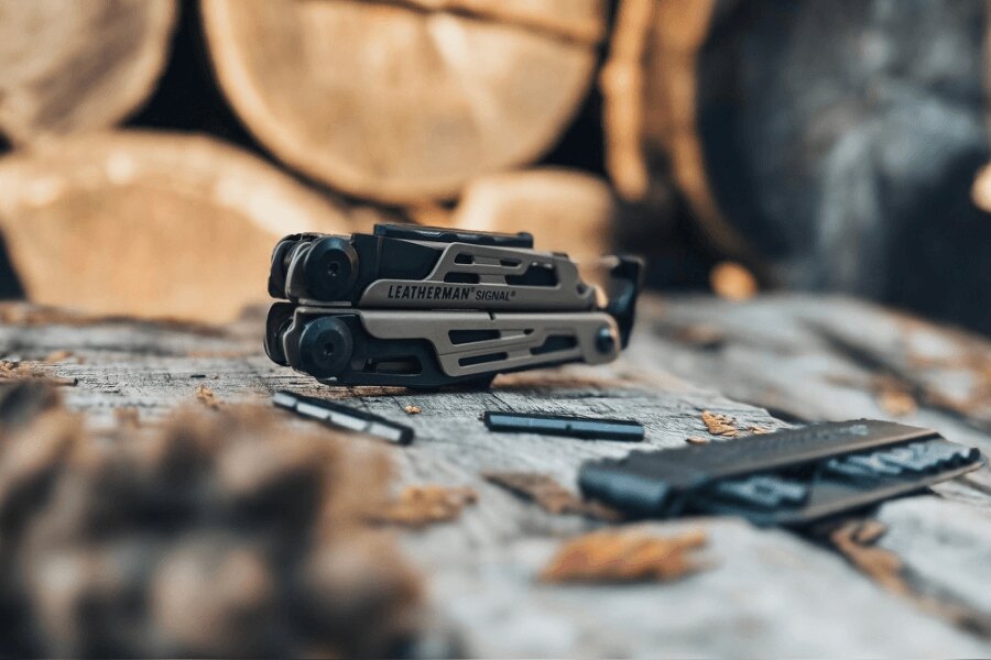 Leatherman Signal așezat pe o masă de lemn cu biți și accesorii într-un mediu outdoor.