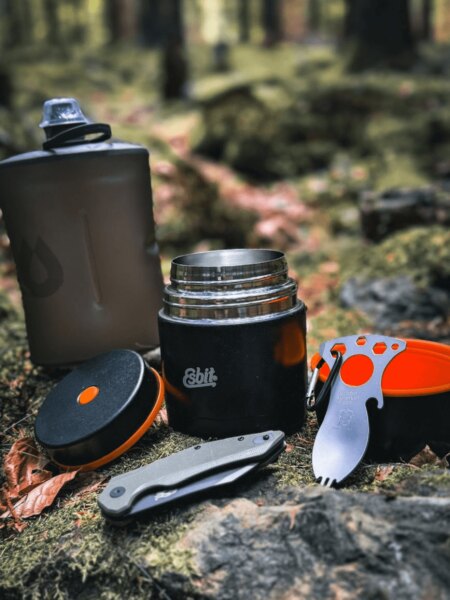 Termosă deschisă pentru mâncare Esbit cu o sticlă pentru outdoor, cuțit pliabil și tacâmuri în pădure.