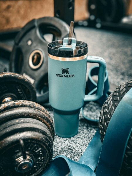 Cana termo Stanley cu pai așezată între gantere și echipamente de fitness.