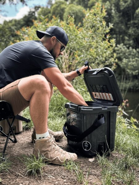 Bărbatul deschide cutia de transport YETI LoadOut GoBox în timpul șederii la apă.