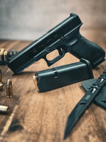 Pistol Glock 17 Gen5 cu cătări mecanice așezată pe masă cu un încărcător, muniție și un cuțit.