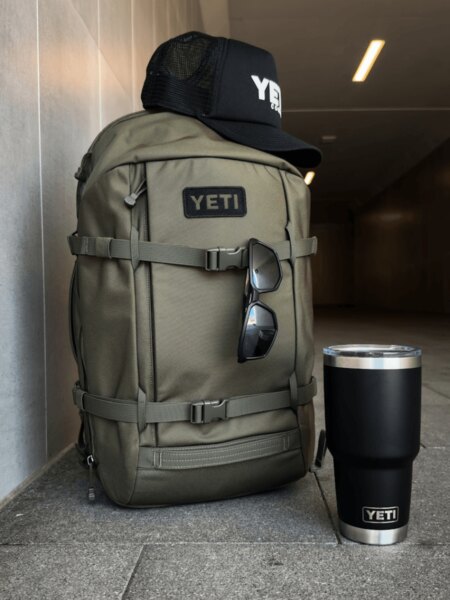 Rucsac YETI Ranchero 27 l gri deschis cu șapcă și sticlă neagră YETI Rambler.